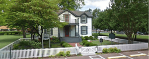 Vintage two-story historic house in Memphis Heritage district with white picket fence, lush greenery, and well-maintained garden, showcasing Memphis's rich architectural and cultural heritage.