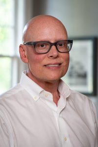 Bald man wearing glasses and a white shirt, smiling indoors, associated with Memphis Heritage Inc.